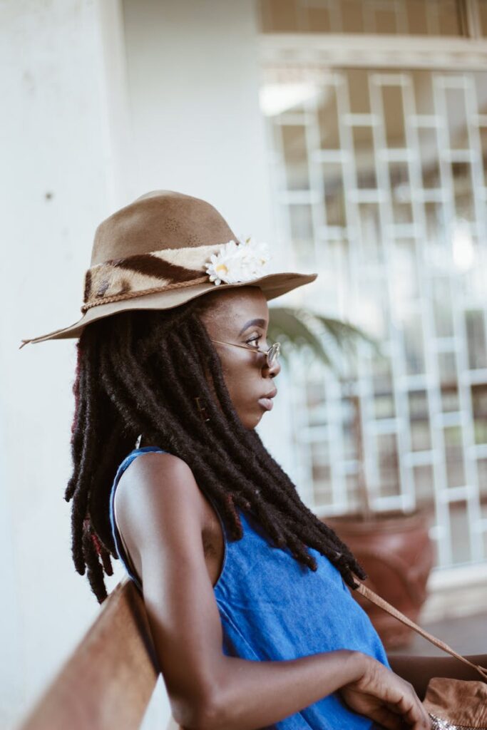 African American woman with dreadlocks wearing a stylish hat sitting outdoors, profile view.